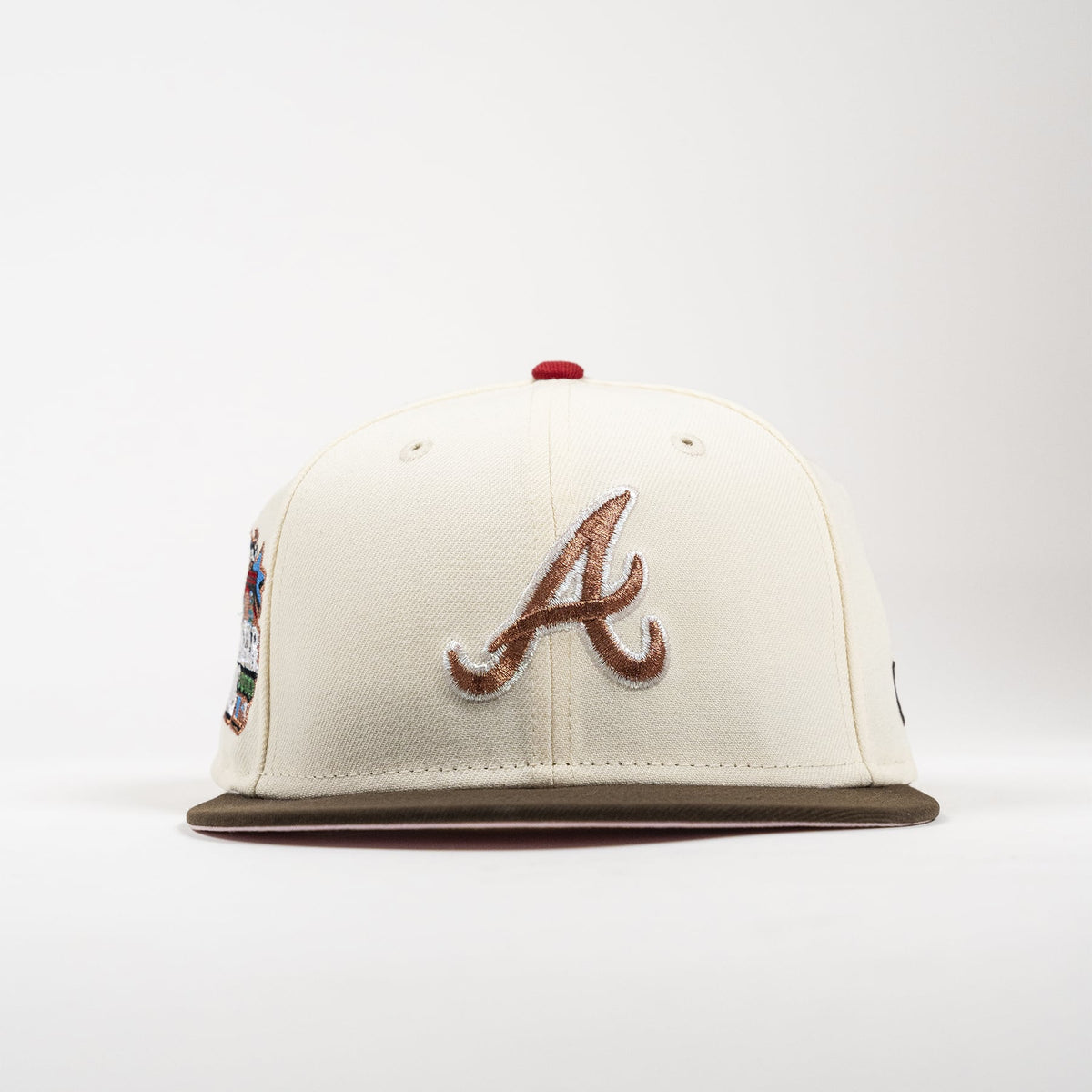 An off-white baseball cap featuring a brown embroidered Atlanta Braves 'A' logo on the front, a brown flat brim, and a small red button on top, shown against a plain white background.