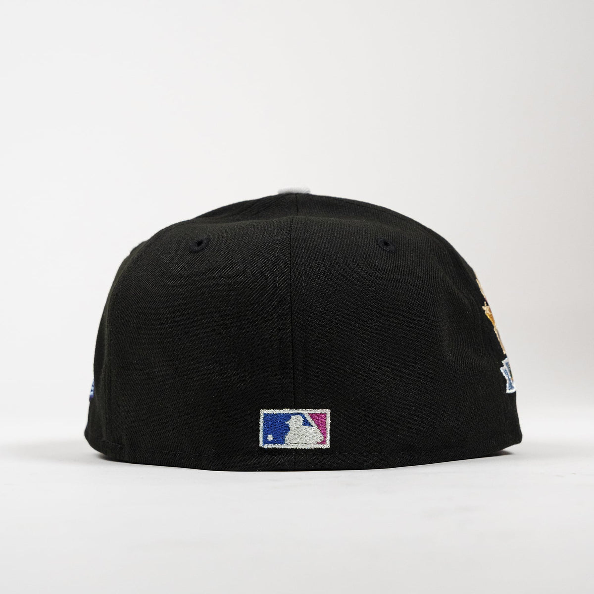 A black baseball cap shown from the back, featuring a silver, blue, and pink MLB logo patch on the center back and a gold and blue embroidered patch on the side, set against a plain white background.