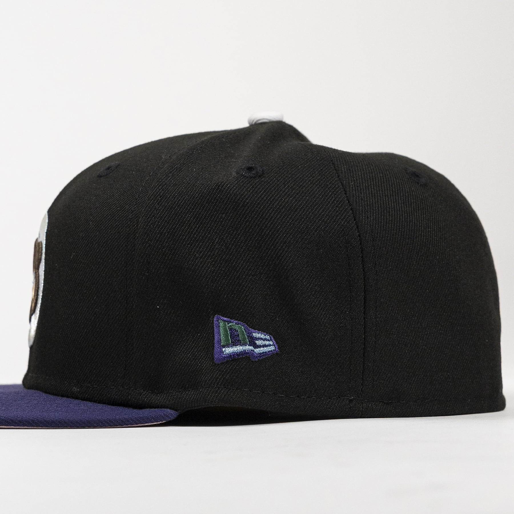 A black structured baseball cap with a dark purple flat brim, featuring a small embroidered New Era flag logo on the side.