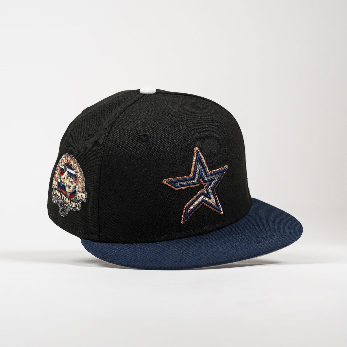 A black Dallas Cowboys 45th Anniversary flat-brim cap with a navy blue visor, featuring an embroidered navy and gold star logo on the front and a commemorative side patch.