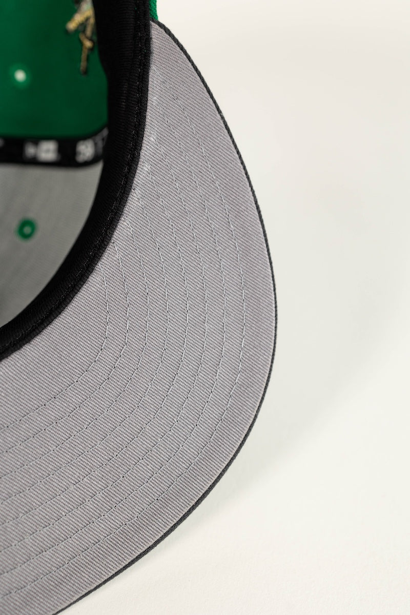 Close-up of a baseball cap showing the gray ribbed brim, black edge trim, and a green interior lining with a small embroidered logo.